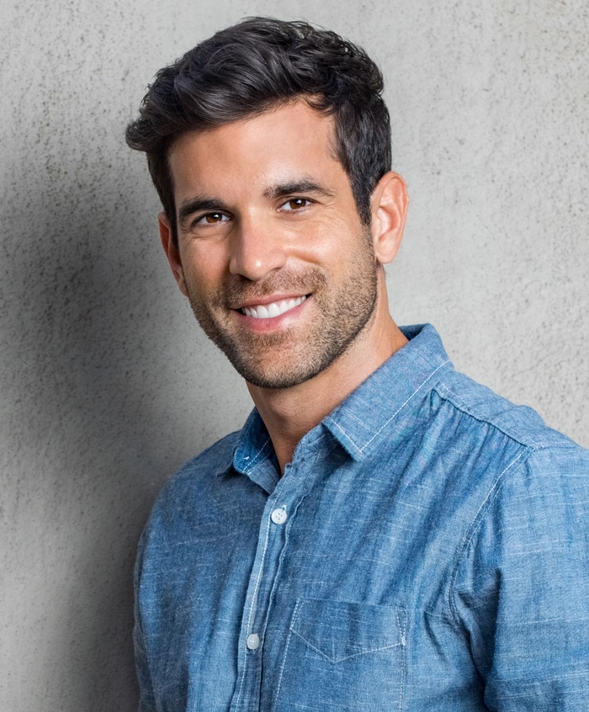 Smiling man in a blue shirt against wall.